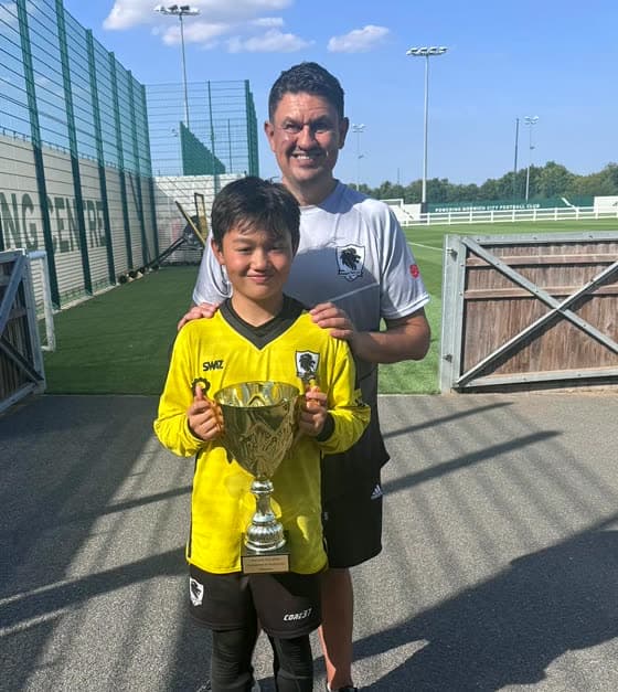James McCall with his son, who is holding a tournament trophy, at a grassroots football ground.