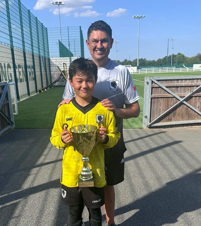 James McCall with his son, who is holding a tournament trophy, at a grassroots football ground.
