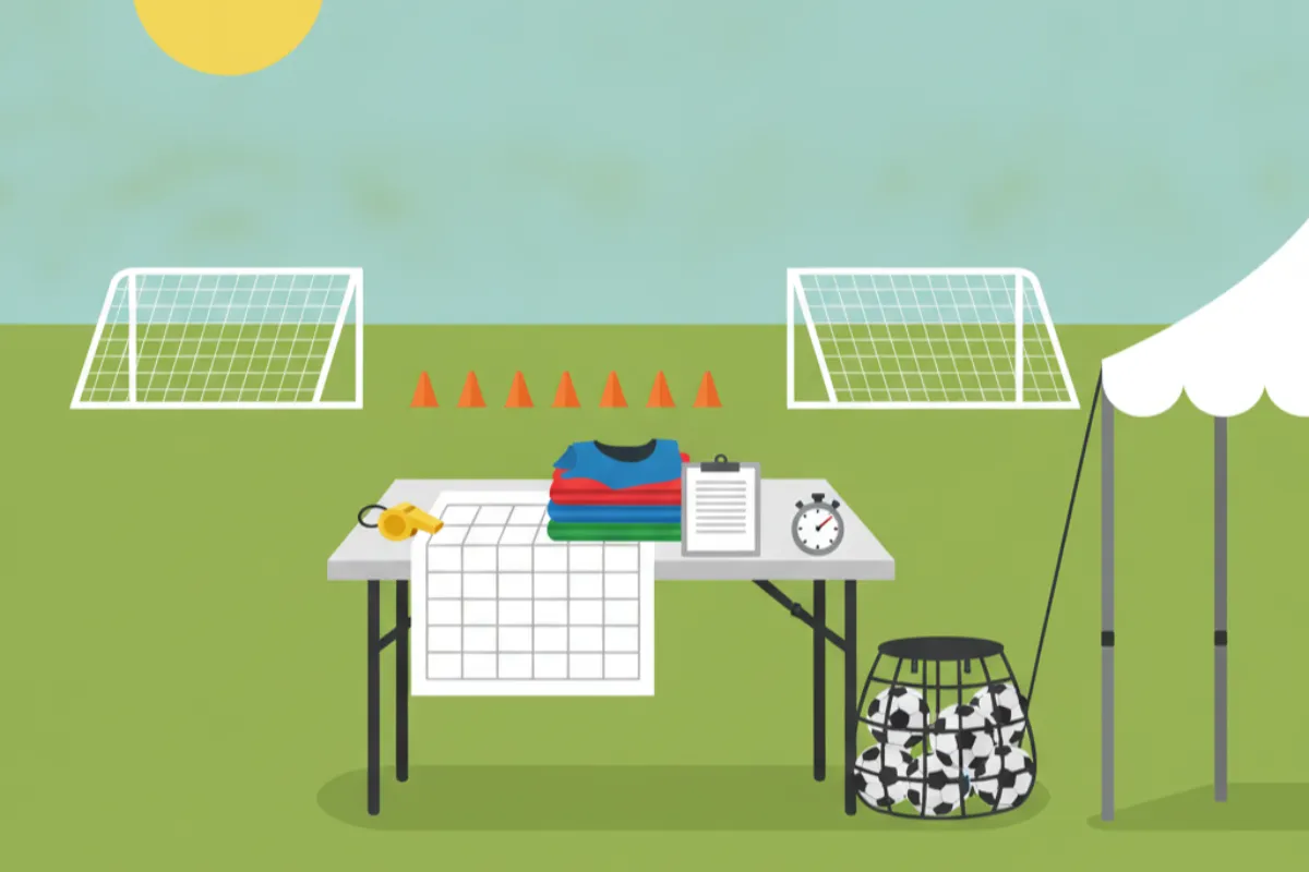 An organiser's table at the pitch edge: a paper schedule weighted by a whistle, coloured bibs, a clipboard, a stopwatch and a bag of footballs, with goals and cones on the grass behind.